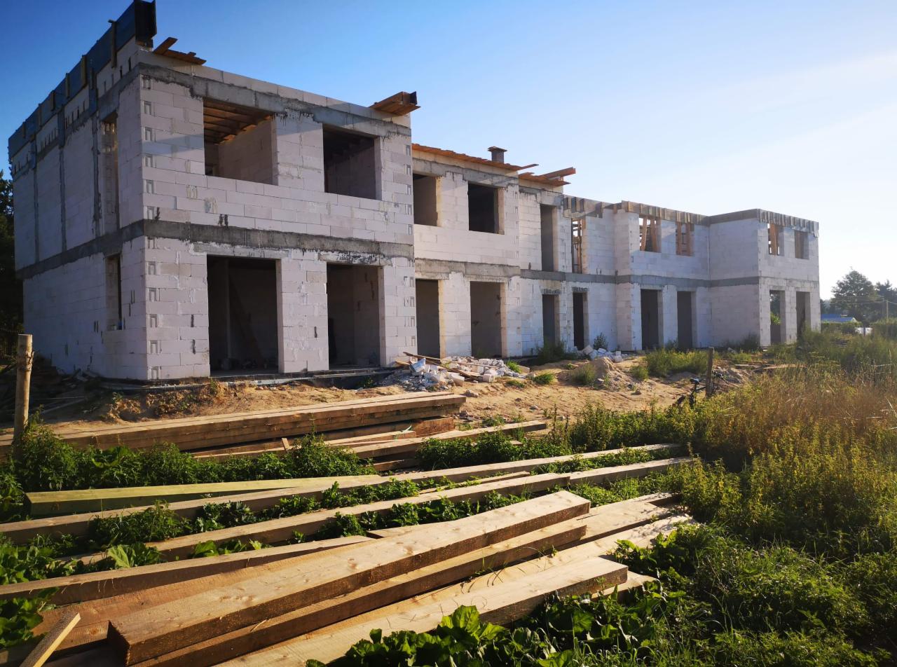 Wczesny etap budowy szeregowca z białych bloczków, widoczne przygotowane deski i otoczenie placu budowy.