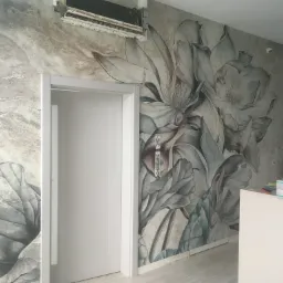 Ściana z fototapetą w kwiaty magnolii w odcieniach szarości i beżu, białe drzwi i klimatyzator sufitowy w pomieszczeniu w trakcie wykańczania, widoczne materiały i narzędzia.