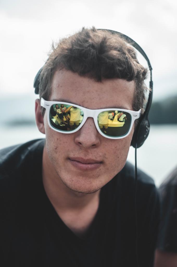 Portret młodego mężczyzny w słuchawkach, z odbiciem grupy ludzi w okularach przeciwsłonecznych.