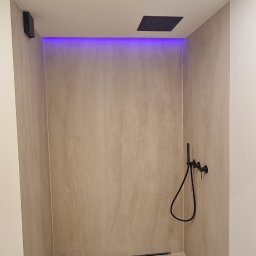 Usługi budowlane Zatorski Krzysztof - Minimalistyczna kabina prysznicowa z czarną armaturą i odpływem liniowym, podświetlona fioletowym światłem LED, wykończona w beżowych odcieniach.