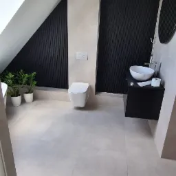 Nowoczesna łazienka na poddaszu z oknem dachowym, czarnymi panelami ściennymi, wiszącą toaletą i umywalką nablatową na czarnej szafce.