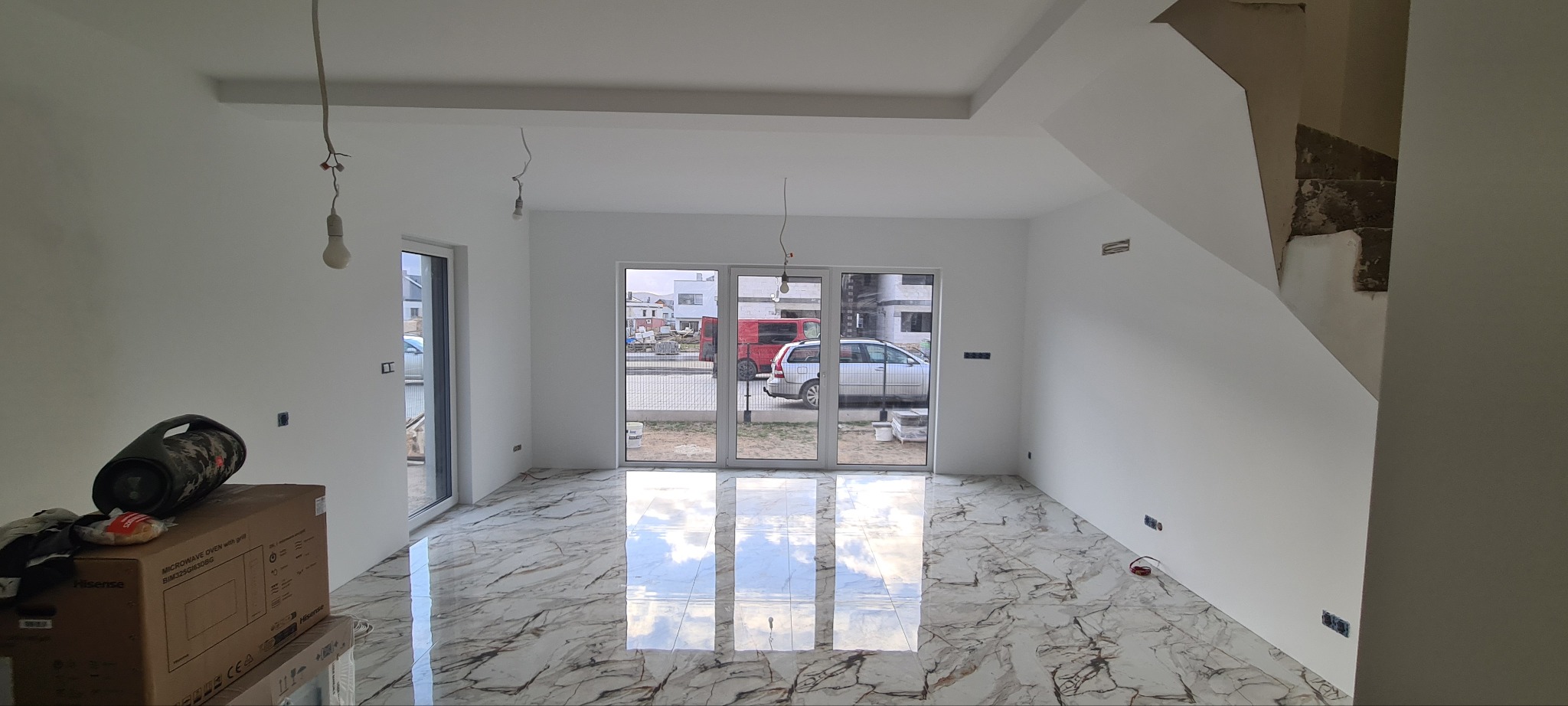 Wnętrze po remoncie: białe ściany, marmurowe płytki podłogowe, widoczne niedokończone schody, na podłodze karton po mikrofalówce i głośnik bluetooth.