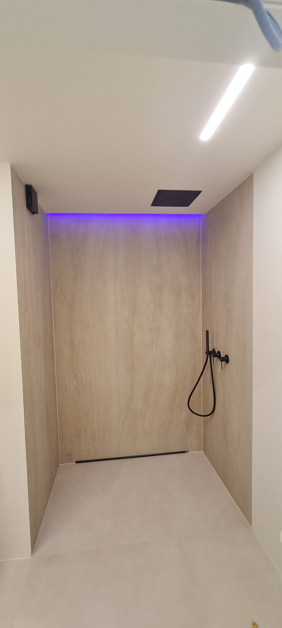 Minimalistyczna kabina prysznicowa z czarną armaturą i odpływem liniowym, podświetlona fioletowym światłem LED, wykończona w beżowych odcieniach.