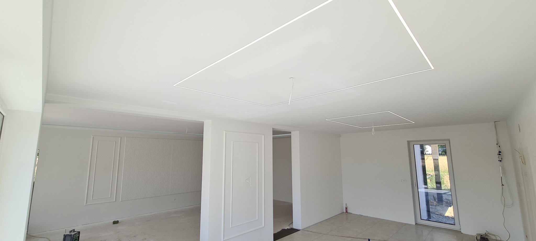 Wykończone wnętrze z białymi ścianami, ozdobnymi panelami ściennymi i podwieszanym sufitem z wbudowanym oświetleniem liniowym.