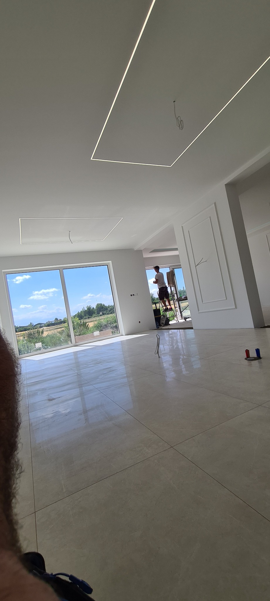 Jasne wnętrze w trakcie wykańczania, widoczny pracownik na drabinie, świeżo pomalowane ściany i sufit z nowoczesnym oświetleniem liniowym.