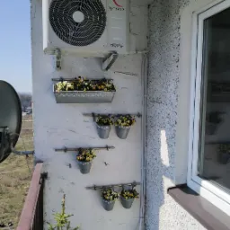 Zewnętrzna jednostka klimatyzacji Rotenso zamontowana na balkonie z kwiatami w ozdobnych doniczkach