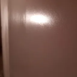 Świeżo pomalowana ściana w odcieniach brązu, z widocznym połyskiem i odbiciem światła, ukazująca gładką powierzchnię.