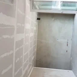 Wnętrze w trakcie remontu: ściany z płyt gipsowo-kartonowych z widocznymi łączeniami, częściowo wykończona ściana z efektem dekoracyjnym, widoczne przewody elektryczne.