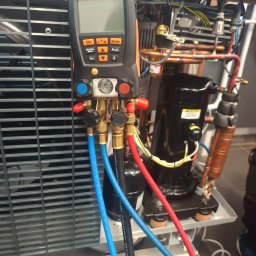 Recohouse - Miernik Testo 557 podłączony do instalacji chłodniczej z widocznym kompresorem i przewodami. Narzędzie diagnostyczne w trakcie pomiarów parametrów pracy układu.