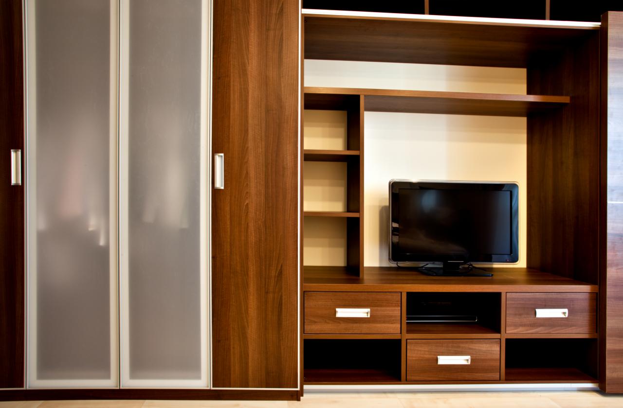 Zabudowa meblowa w salonie z szafą z przesuwnymi drzwiami z mlecznego szkła i regałem z miejscem na telewizor, wykończona w odcieniach brązu.