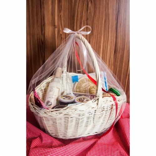 Biały wiklinowy kosz z kokosowym likierem, dżemami i ciasteczkami, owinięty tiulem i przewiązany czerwoną wstążką, na czerwono-białej kraciastej tkaninie i tle z drewnianych paneli.