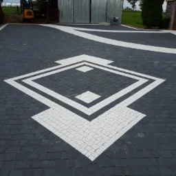 Ułożona kostka brukowa w geometryczny wzór z czarnych i białych kostek, z minikoparką i zagęszczarką w tle.