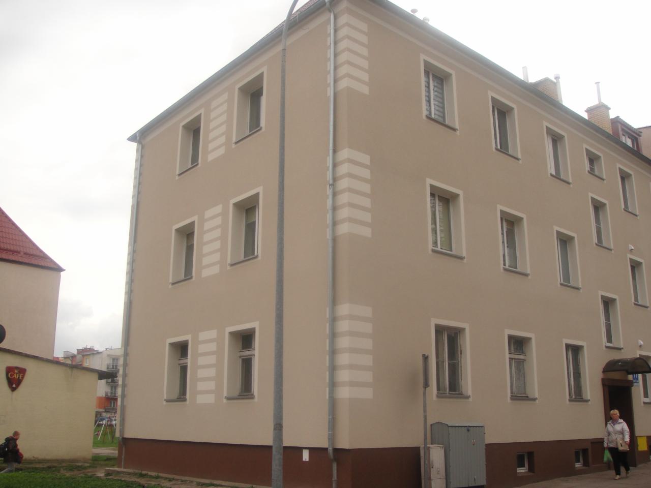 Budynek wielorodzinny po renowacji elewacji z dekoracyjnymi pasami w kolorze jasnego beżu, widoczne okna z białymi ramami i cokół w kolorze ciemnego brązu.