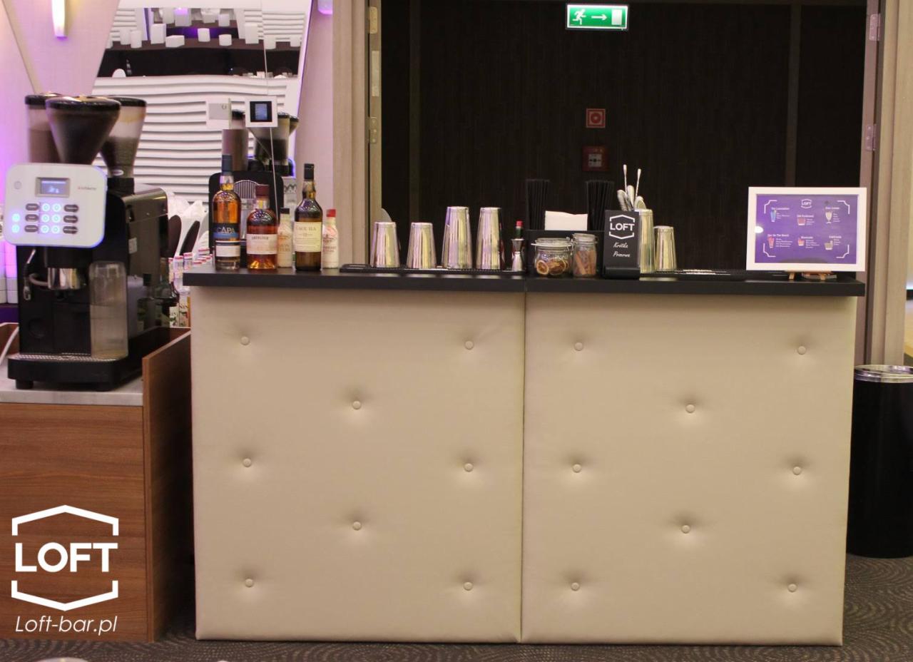 Mobilny bar z beżowym panelem pikowanym, ekspres do kawy, butelki alkoholi i akcesoria barmańskie na blacie.