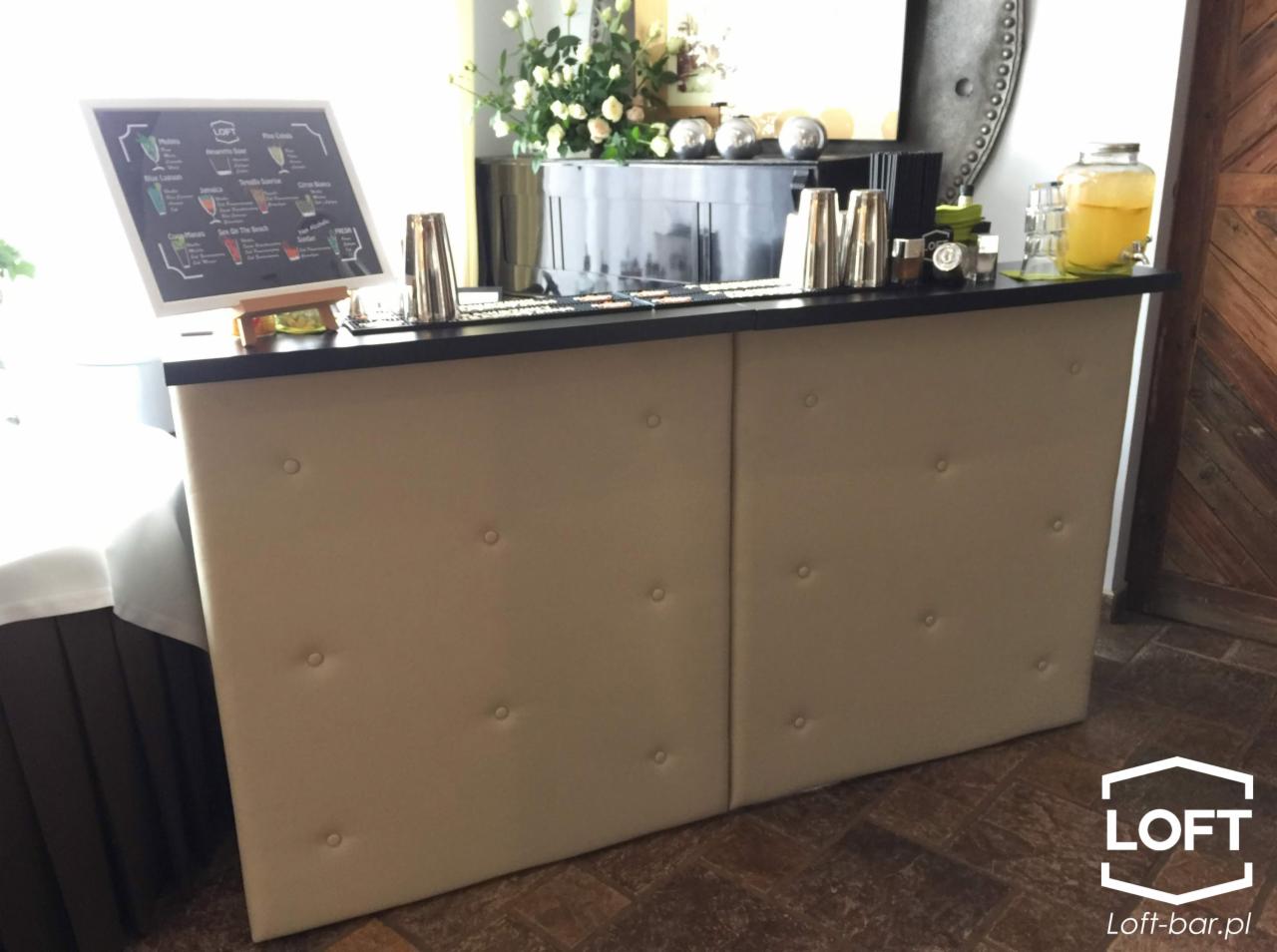 Mobilny bar z beżowym, pikowanym frontem, menu drinków na tablicy i akcesoriami barmańskimi, gotowy do obsługi wydarzenia w Krakowie.