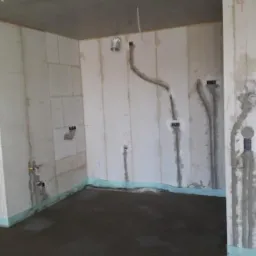 Surowy stan wnętrza z widocznymi bruzdami pod instalacje elektryczne i hydrauliczne w ścianach z betonu komórkowego, świeżo wylana podłoga, zabezpieczenie przeciwwilgociowe przy podłodze.