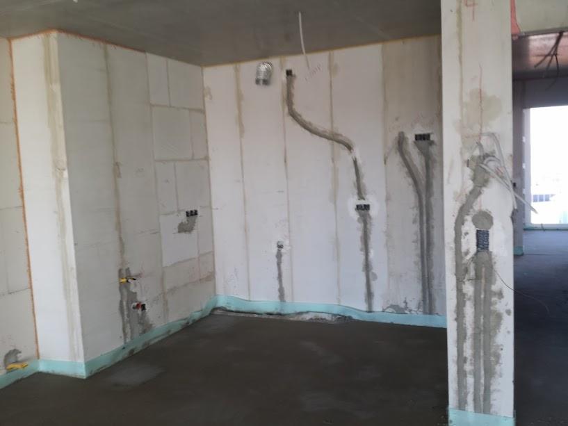 Surowy stan wnętrza z widocznymi bruzdami pod instalacje elektryczne i hydrauliczne w ścianach z betonu komórkowego, świeżo wylana podłoga, zabezpieczenie przeciwwilgociowe przy podłodze.