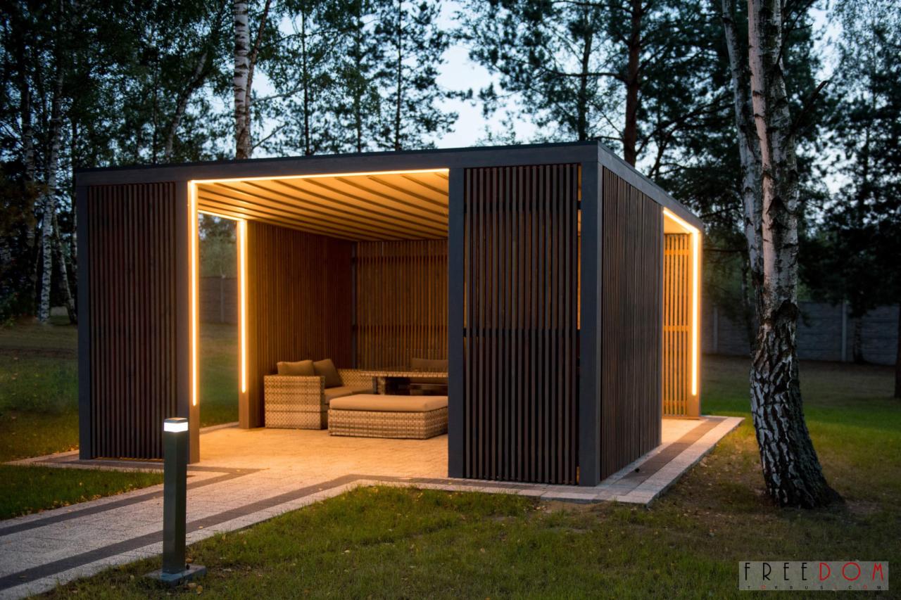 Nowoczesna, drewniana konstrukcja z oświetleniem LED, wyposażona w rattanowe meble ogrodowe, na tle drzew i trawnika.