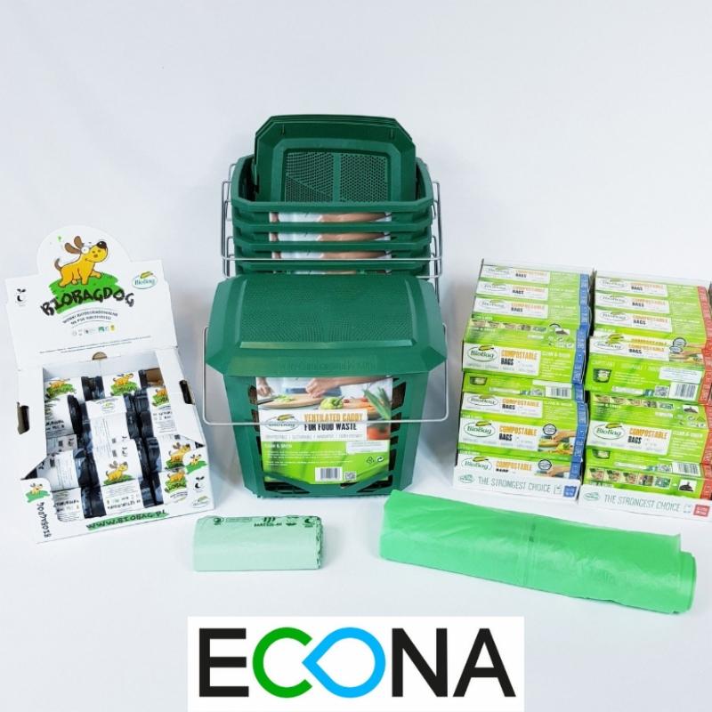 Zestaw do segregacji odpadów organicznych BioBag Dog: zielony pojemnik z uchwytem, wkłady, rolki biodegradowalnych worków na śmieci oraz kartonowy display z logo i produktami firmy.