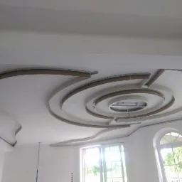 Sufit z dekoracyjną konstrukcją z płyt kartonowo-gipsowych w kształcie spirali, widoczne elementy montażowe i przygotowanie pod oświetlenie, wnętrze w trakcie prac wykończeniowych.