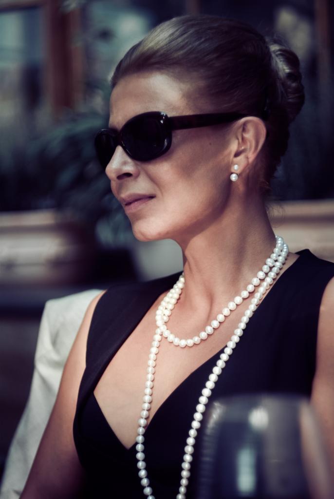 Portret kobiety w czarnej sukience i okularach przeciwsłonecznych, z perłami, wykonany w Trzebini. Subtelny makijaż i elegancka fryzura.