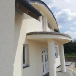 Bud-Tynk - Elewacja domu jednorodzinnego z okrągłym balkonem, widoczna faktura tynku i elementy wykończeniowe.