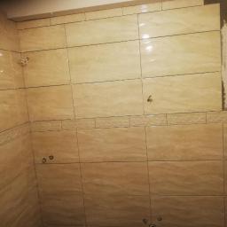 Bud-Tynk - Montaż beżowych płytek imitujących marmur w łazience, widoczne niedokończone fragmenty ściany i dekoracyjny pas płytek.