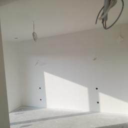 Bud-Tynk - Wnętrze pokoju po szpachlowaniu i malowaniu na biało, widoczne przygotowane otwory na gniazdka elektryczne i wystające kable ze ściany i sufitu.