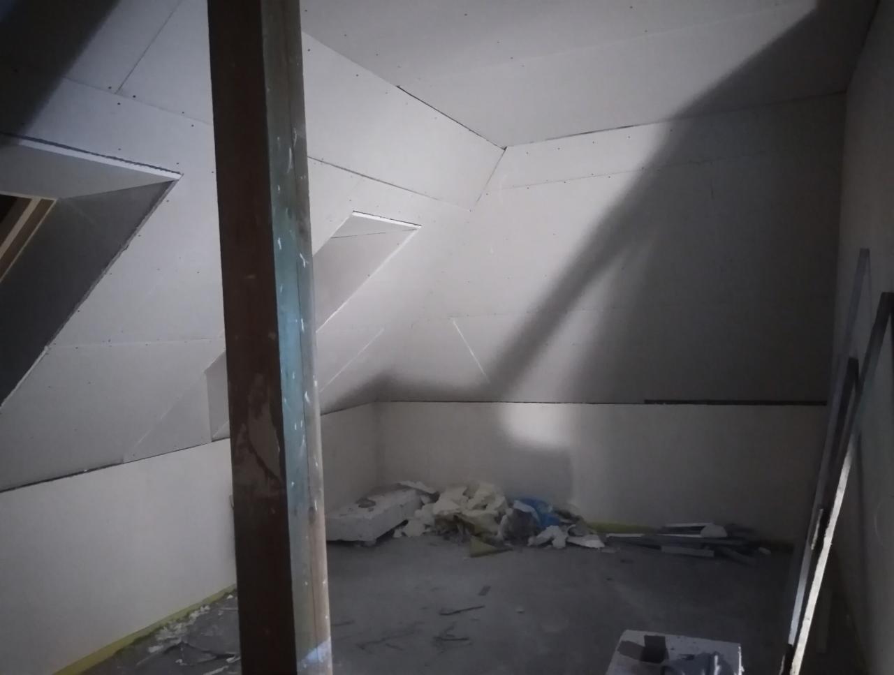 Poddasze w trakcie adaptacji: widoczne płyty na skosach dachu, drewniany słup konstrukcyjny i izolacja termiczna na podłodze.