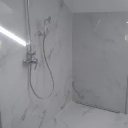 Wykończona kabina prysznicowa z chromowaną armaturą i białymi płytkami imitującymi marmur, z widocznym odpływem liniowym w podłodze.