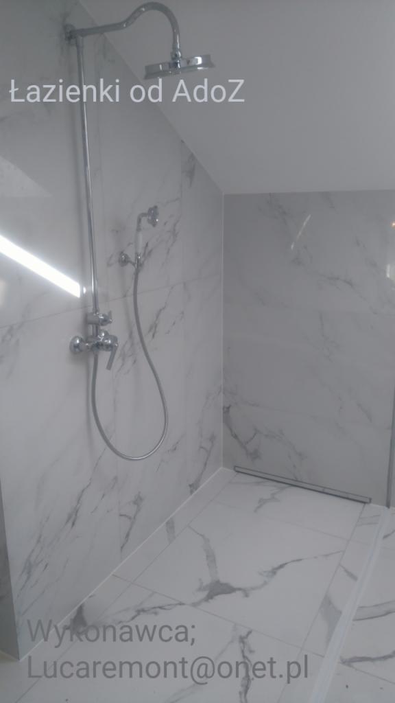 Wykończona kabina prysznicowa z chromowaną armaturą i białymi płytkami imitującymi marmur, z widocznym odpływem liniowym w podłodze.