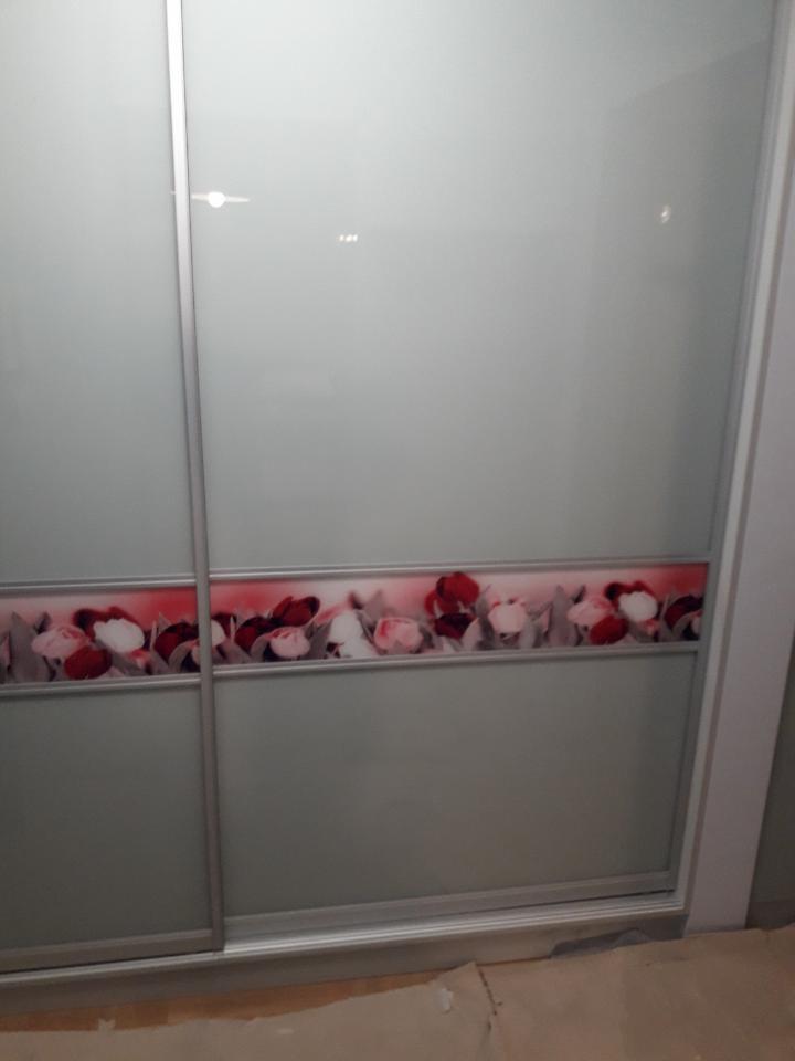 Szafa przesuwna z matowymi drzwiami, ozdobiona poziomym paskiem z motywem czerwono-białych kwiatów, widoczne aluminiowe prowadnice.