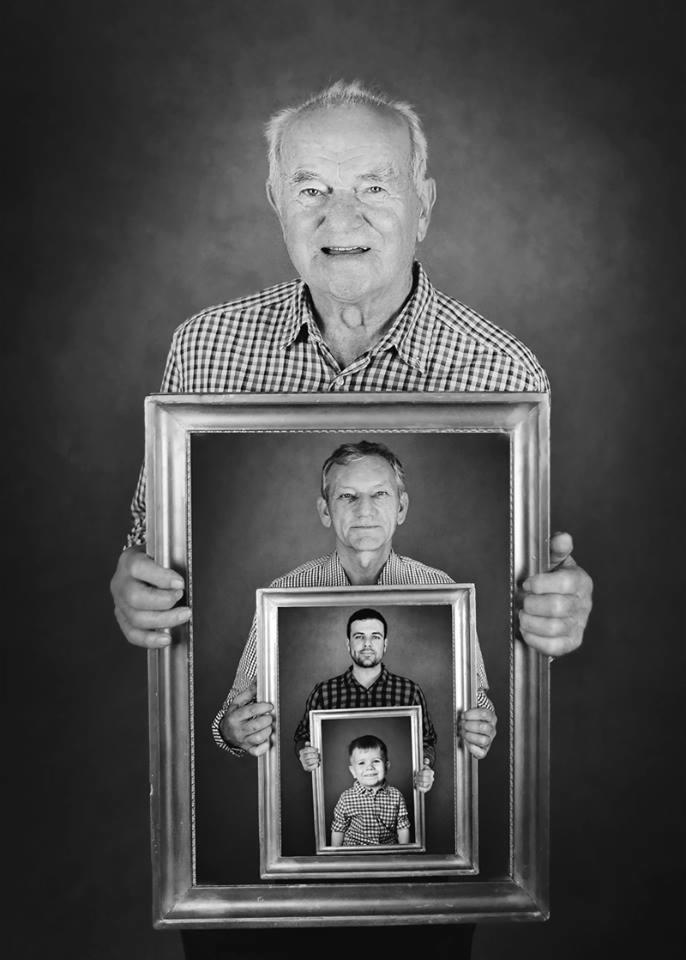 Czarno-białe portretowe ujęcie mężczyzny trzymającego w rękach ramę ze zdjęciem młodszego mężczyzny, który z kolei trzyma ramę ze zdjęciem małego chłopca, wszyscy w podobnych koszulach w kratę,...