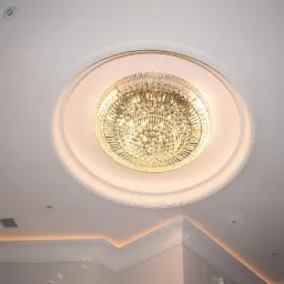 Kryształowy żyrandol w okrągłej wnęce sufitowej, otoczony profilowanym gzymsem z subtelnym podświetleniem LED, uzupełniony punktowymi lampami halogenowymi.