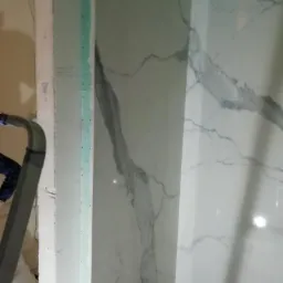 Montaż płytek imitujących marmur w narożniku łazienki, widoczne fragmenty drabiny i resztki zaprawy.