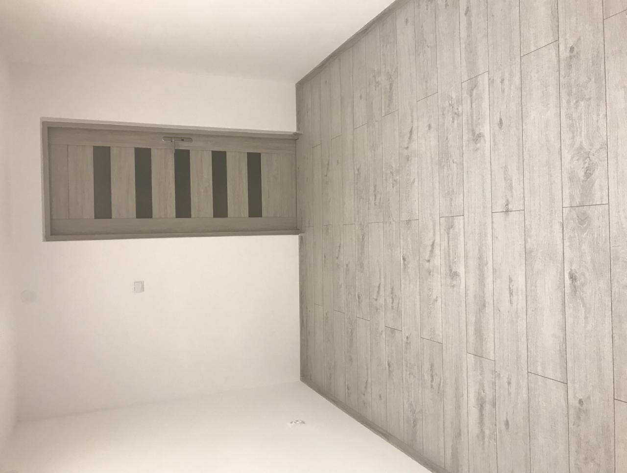 Wnętrze pokoju po remoncie z jasną podłogą imitującą drewno i zamontowanymi szarymi drzwiami z przeszkleniami.