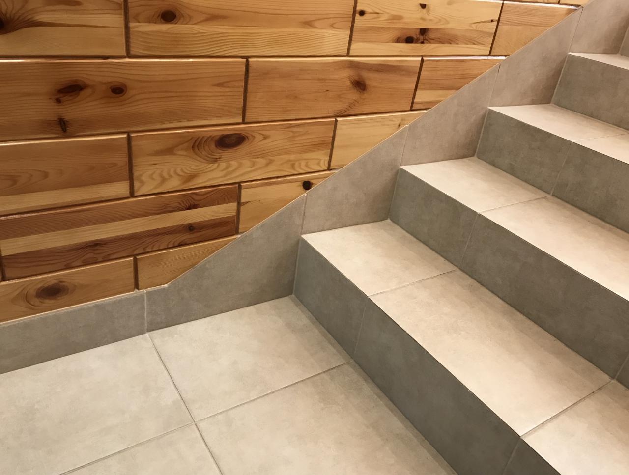 Wykończone schody z jasnych płytek ceramicznych, przylegające do ściany z drewnianych paneli o ciepłym odcieniu brązu, z widocznymi słojami i sękami.