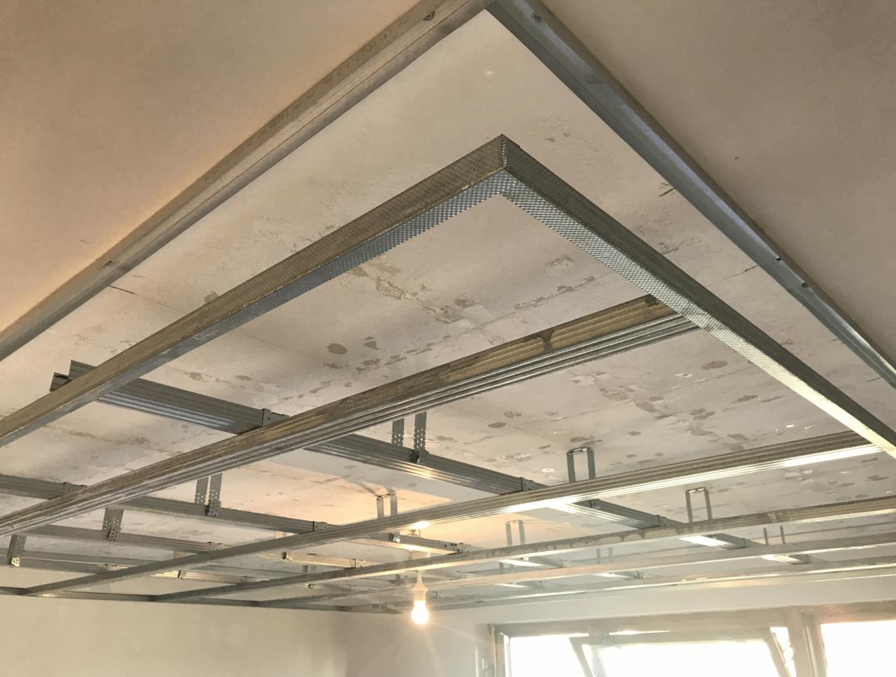 Metalowy stelaż sufitowy z profili aluminiowych, przygotowany do montażu płyt karton gips, widoczne mocowania i surowy betonowy strop w tle.