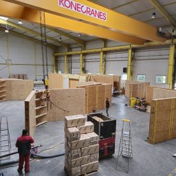 BUDLEP SPÓŁKA Z OGRANICZONĄ ODPOWIEDZIALNOŚCIĄ - Montaż ścian domu szkieletowego w hali produkcyjnej z użyciem suwnicy Konecranes. Widoczne elementy konstrukcyjne, materiały izolacyjne Steico i pracownicy.