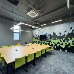 BUDLEP SPÓŁKA Z OGRANICZONĄ ODPOWIEDZIALNOŚCIĄ - Nowoczesna sala konferencyjna z długim stołem, zielonymi krzesłami i dekoracyjną ścianą w geometryczne wzory. Widoczna klimatyzacja kasetonowa pod sufitem.