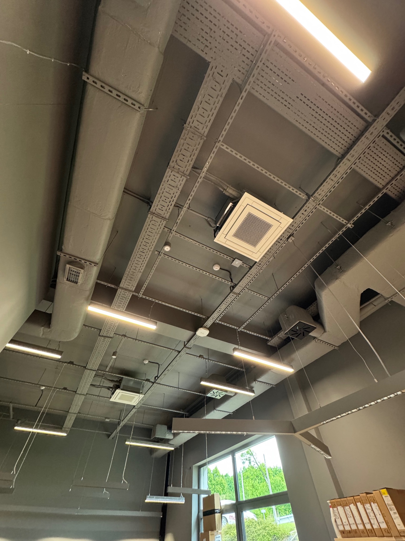 Sufit biurowy w Świętochłowicach z zamontowanymi panelami klimatyzacyjnymi, oświetleniem liniowym i instalacjami podwieszonymi na szynach. Widok z dołu.