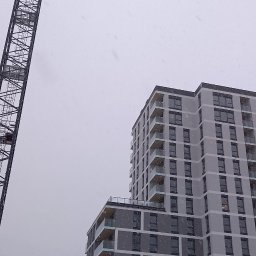 Pol-Bud Professional - Budynek wielorodzinny w trakcie budowy, widziany z dołu w zimowy dzień. Na pierwszym planie żuraw budowlany i elementy konstrukcyjne.