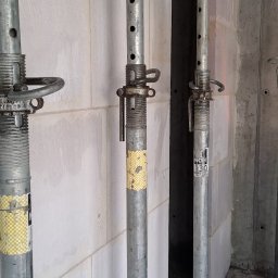 Pol-Bud Professional - Wznoszenie ściany z bloczków z betonu komórkowego, podpartej metalowymi stemplami budowlanymi. Widoczne spoiny i niedoskonałości, surowy stan budowy.