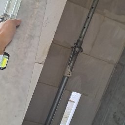 Pol-Bud Professional - Wznoszenie ściany z betonu komórkowego, podpora stalowa, poziomica w użyciu. Widoczny fragment stropu i pustak wentylacyjny. Praca w toku, surowy stan.