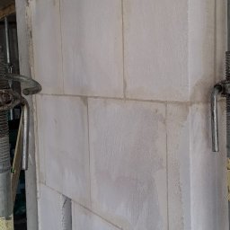 Pol-Bud Professional - Ściana z białych bloczków, widoczne spoiny i podpory budowlane. Fragment ściany z otworem. Surowy stan, budowa w toku. Bliskie ujęcie.