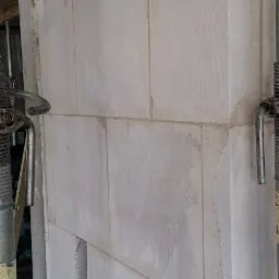 Ściana z białych bloczków, widoczne spoiny i podpory budowlane. Fragment ściany z otworem. Surowy stan, budowa w toku. Bliskie ujęcie.