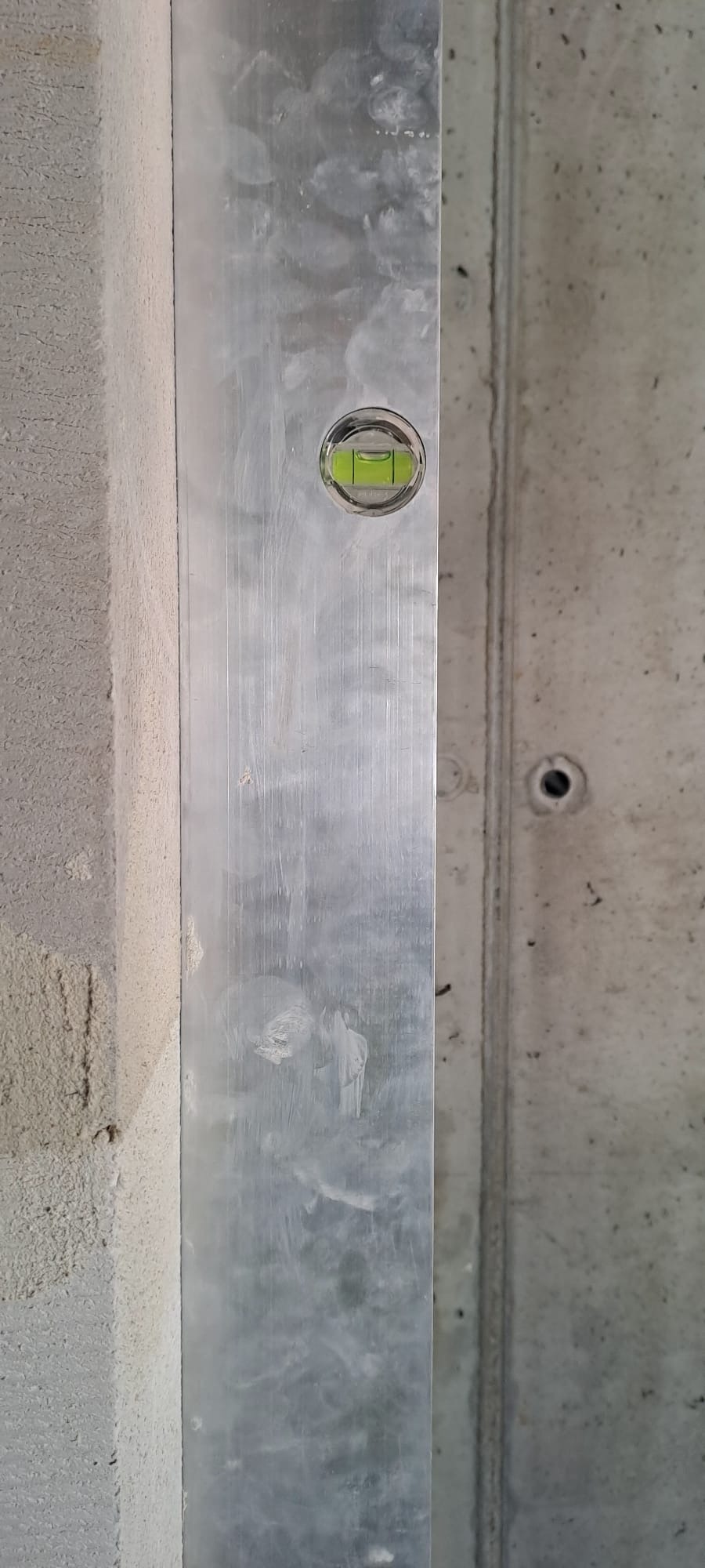 Pionowy poziomica na surowej ścianie z betonu komórkowego, kontrola pionu, widoczne ślady po szpachlowaniu. Szary odcień betonu.