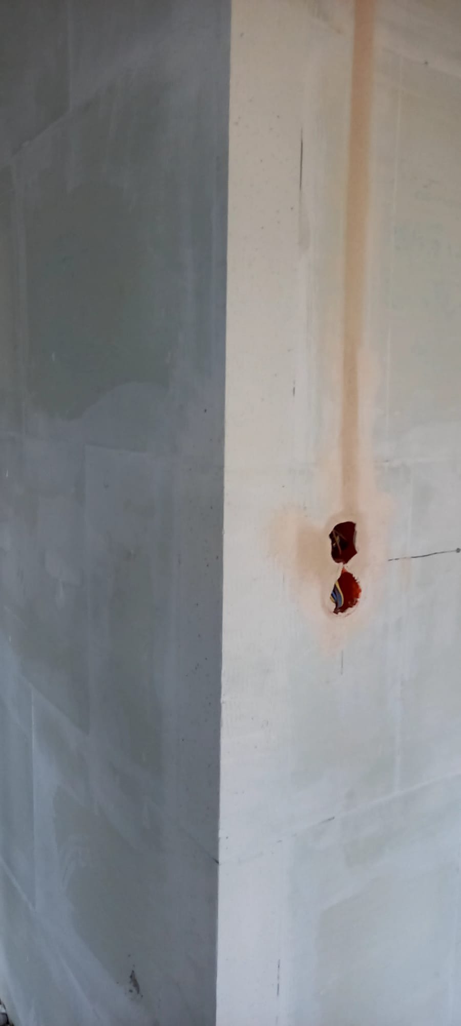 Narożnik ścian po szpachlowaniu, widoczne puszki elektryczne z przewodami. Ściana po lewej w szarym odcieniu, po prawej jaśniejsza, przygotowana pod malowanie.