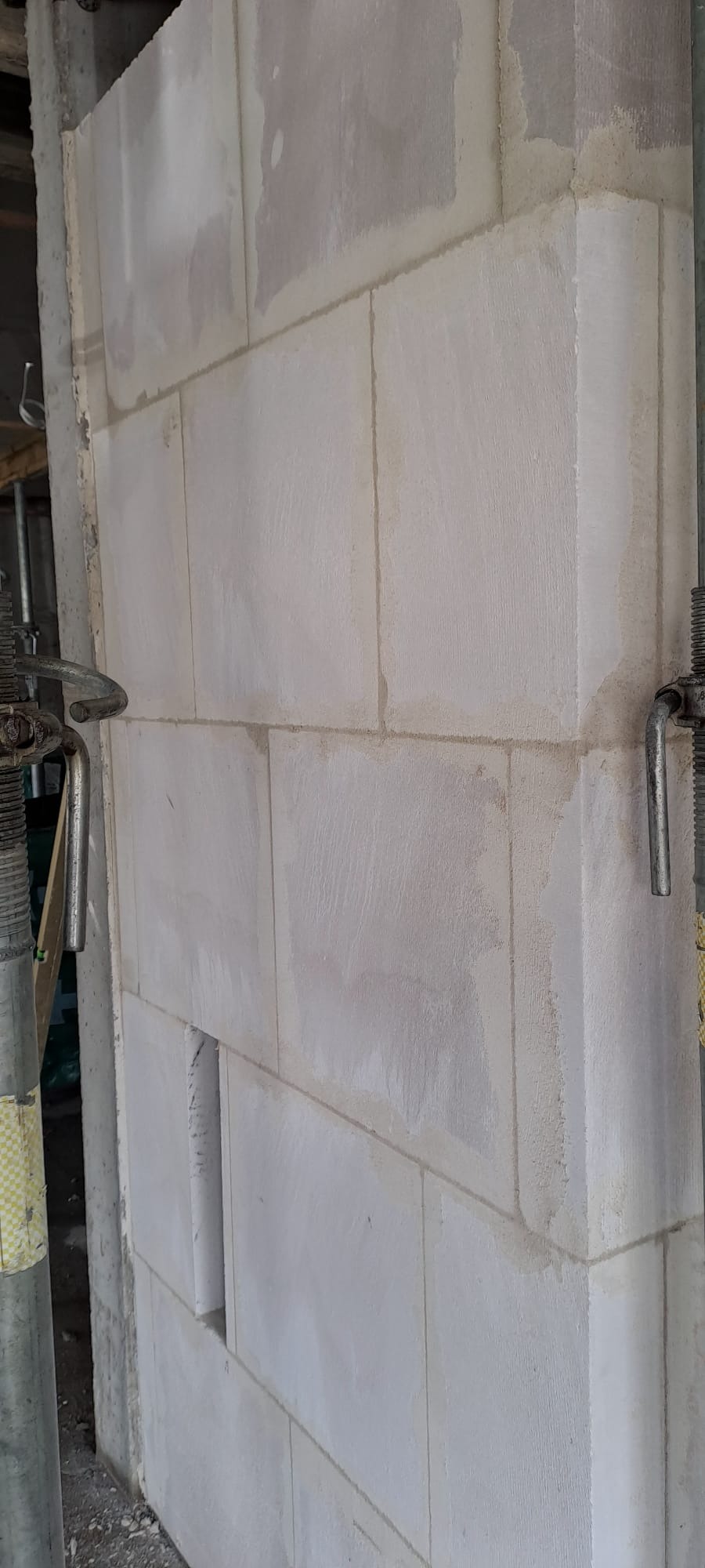 Ściana z białych bloczków, widoczne spoiny i podpory budowlane. Fragment ściany z otworem. Surowy stan, budowa w toku. Bliskie ujęcie.