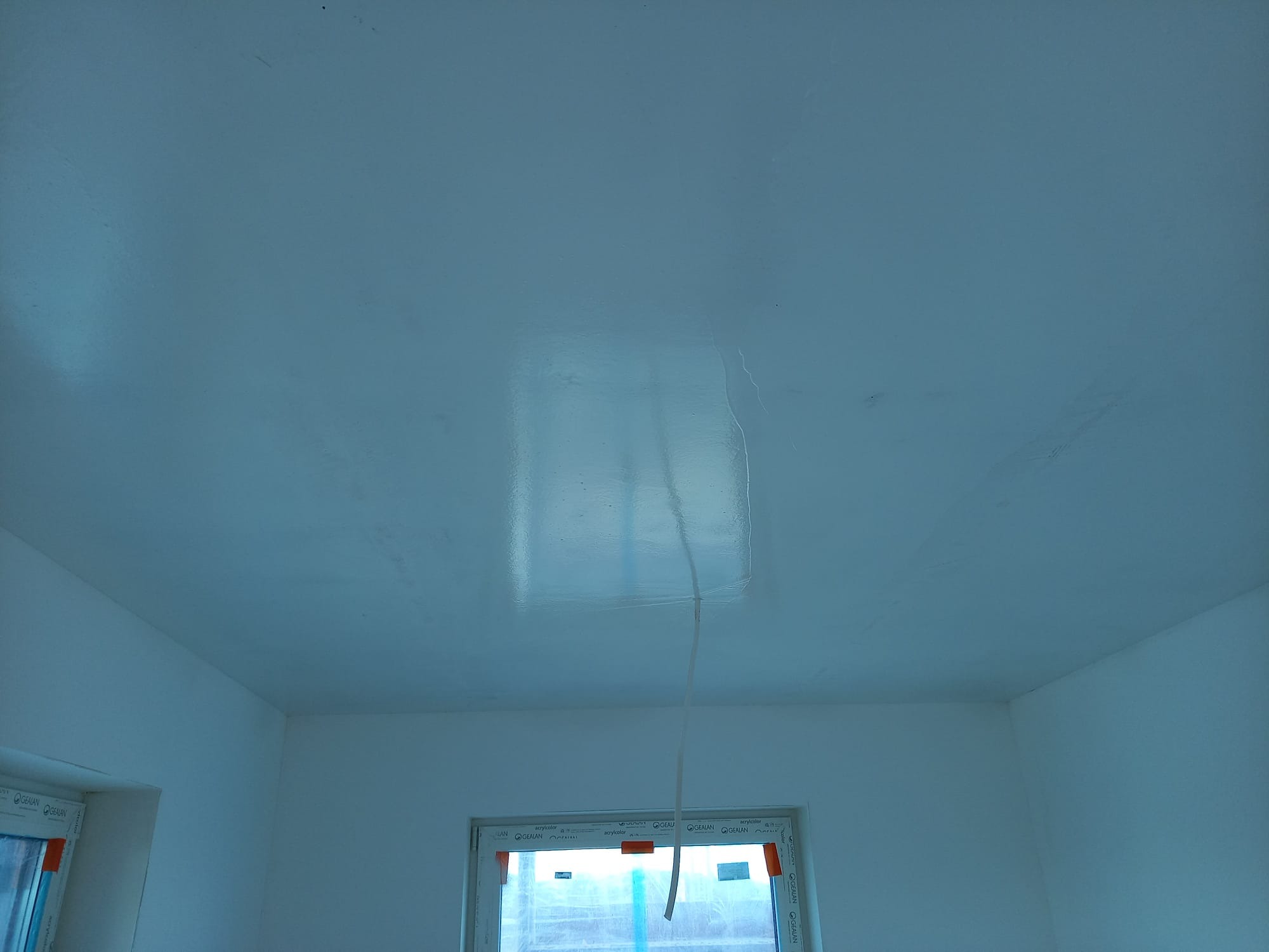 Gładki, świeżo pomalowany sufit w jasnym odcieniu, widoczne okna z ramami. Minimalistyczne wnętrze po remoncie, gotowe do dalszego wykończenia.